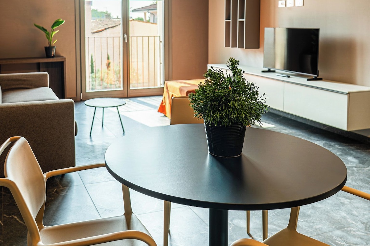 A modern living room with a round table, two chairs, a sofa, a television, and a balcony with a view.