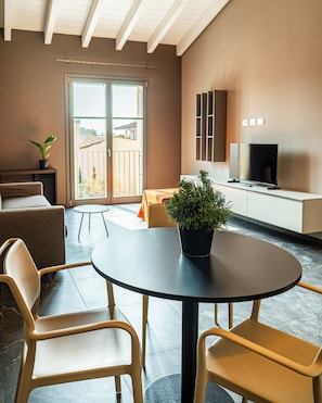 A modern living room with a round table, two chairs, a sofa, a television, and a balcony with a view.