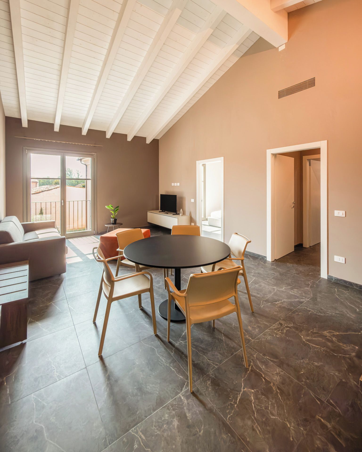 A spacious living area with a high ceiling, a round dining table, and modern furniture.
