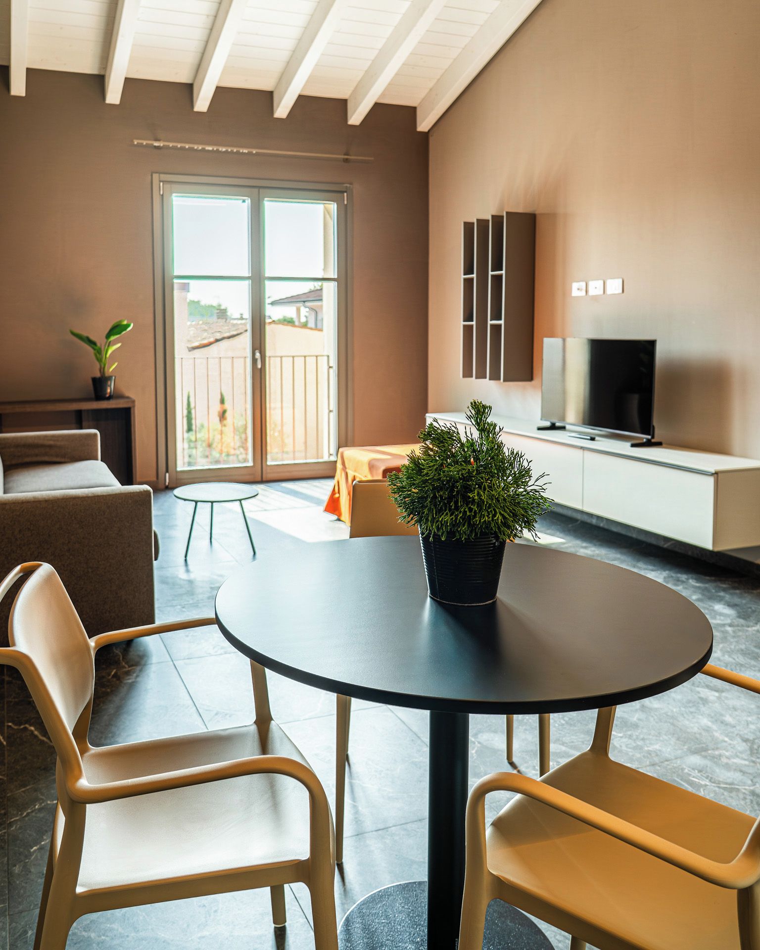 A modern living room with a round table, two chairs, a sofa, a television, and a balcony with a view.