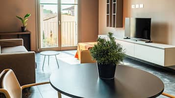 A modern living room with a round table, two chairs, a sofa, a television, and a balcony with a view.