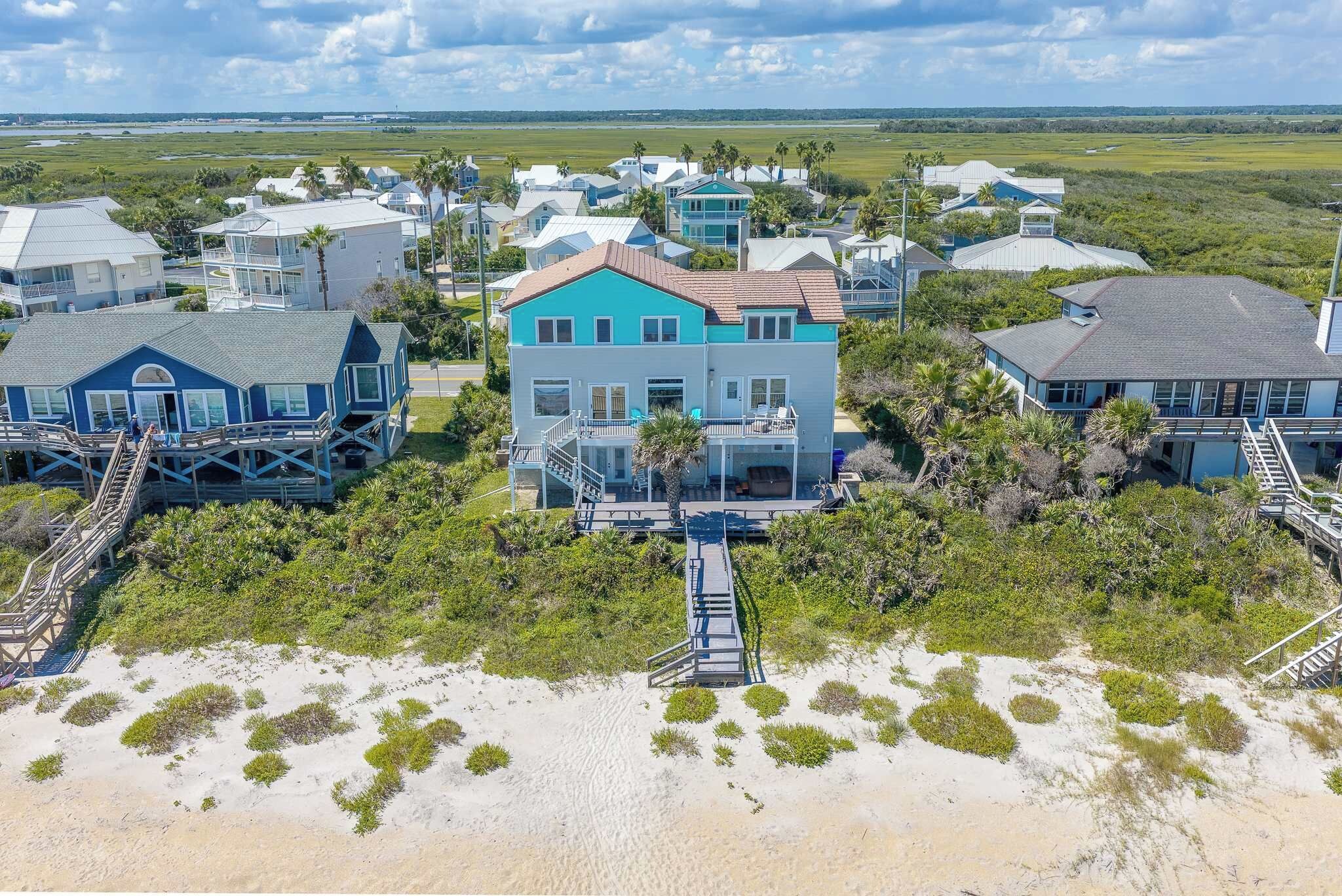 A coastal residential area with multiple houses, a beach in the foreground, and a clear view of the ocean in the background.