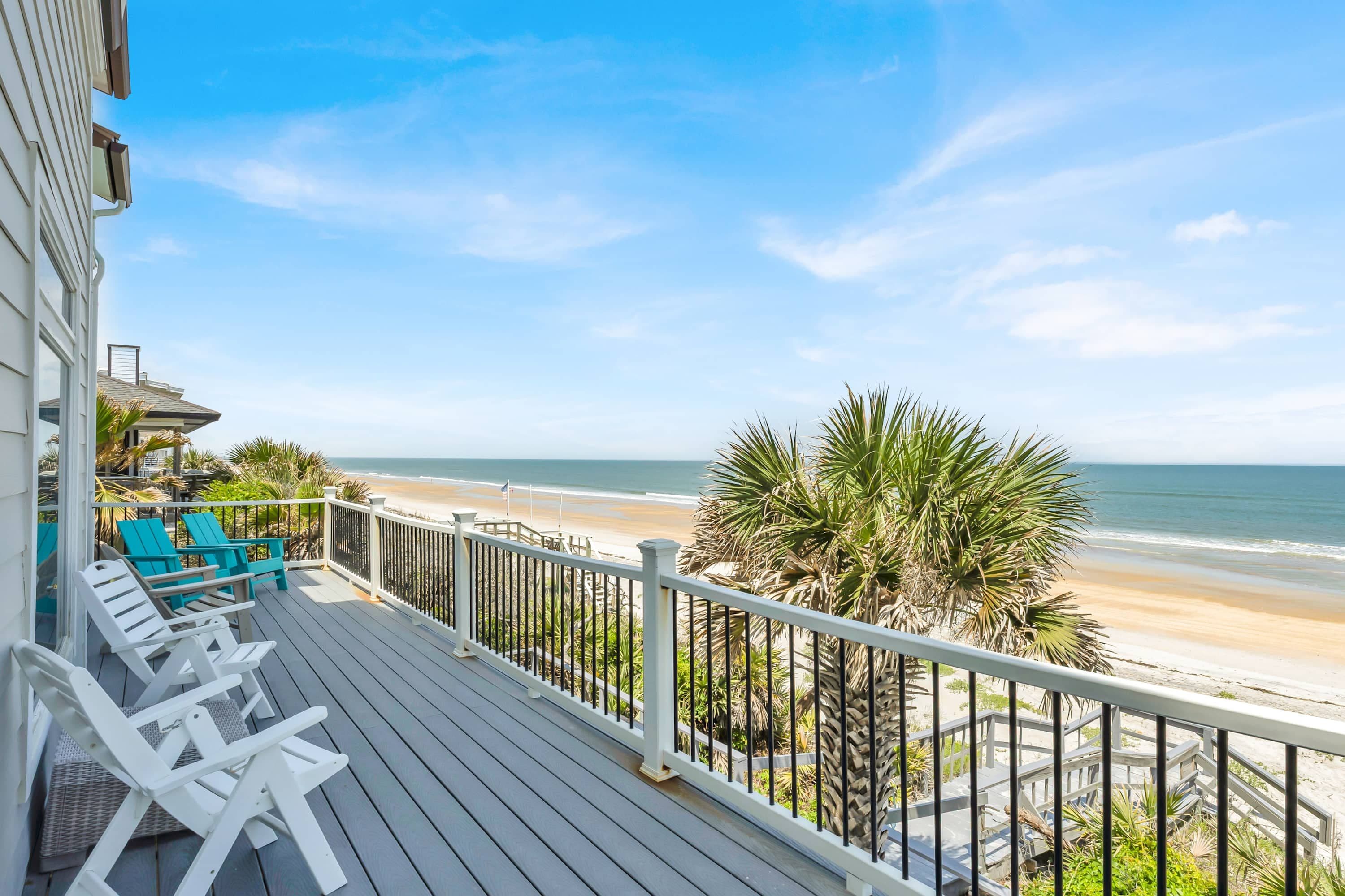 A wooden deck with white railings overlooking a beach.