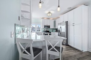 A modern kitchen with white cabinetry, a central island, and pendant lighting. - Seascape l Oceanfront l Hot Tub l Game Room (St. Johns County)