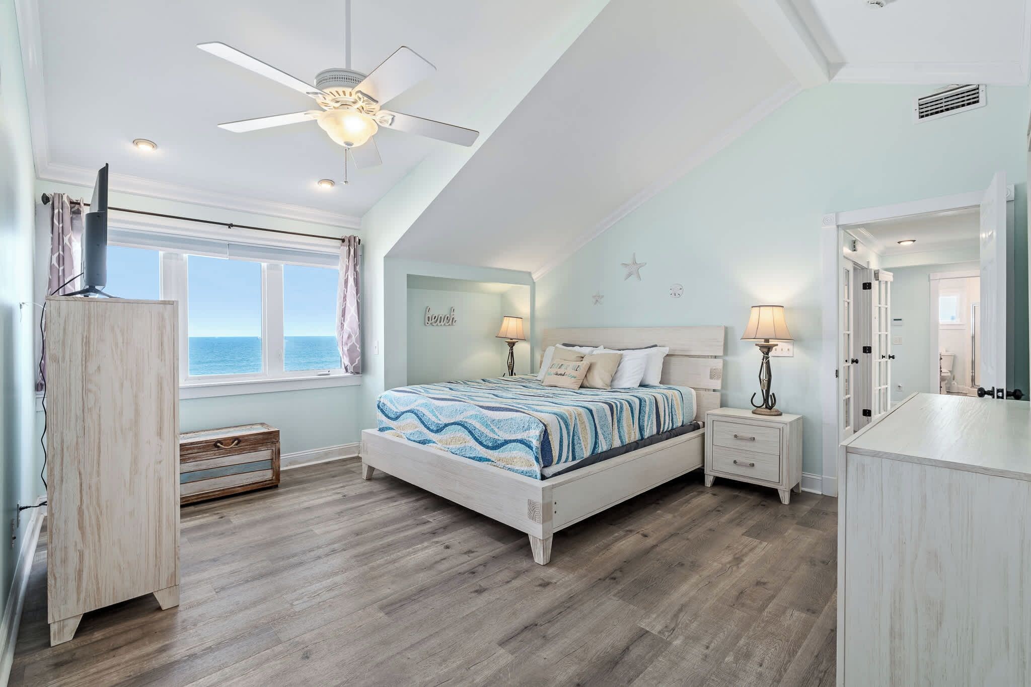 A bedroom with a bed, bedside tables, a ceiling fan, a window with a view, and a wardrobe.