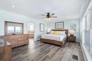 Quarto com cama de madeira, cômoda, ventoinha no teto e janela com persianas.
