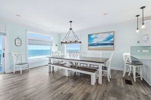A dining area with a view of the ocean, a large painting, and a modern pendant light. - Seascape l Oceanfront l Hot Tub l Game Room (St. Johns County)