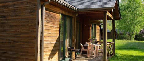 A wooden cabin with a covered porch, a table with chairs, and a view of the surrounding greenery.
