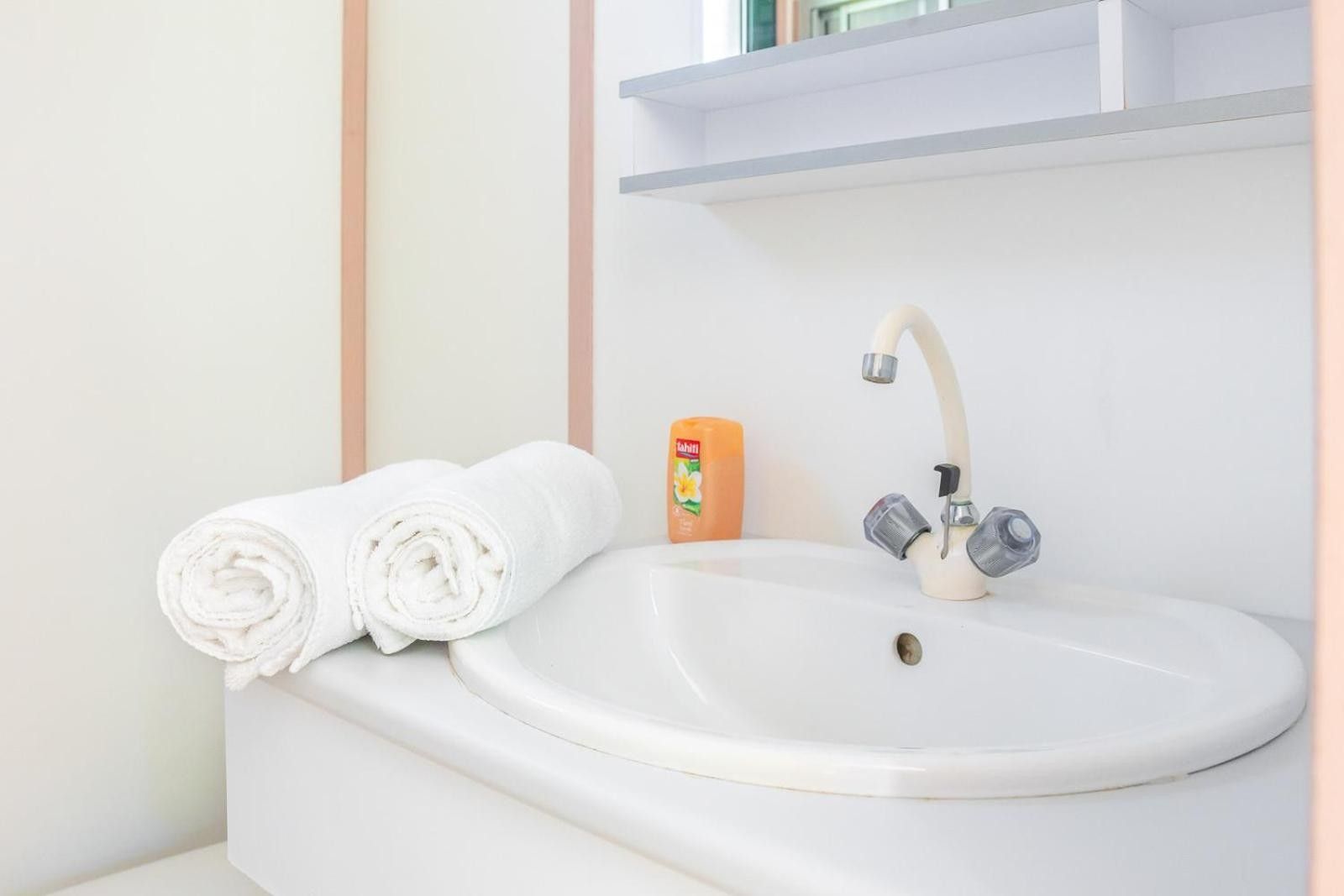 A bathroom with a white sink, two rolled towels, and a bottle of soap.