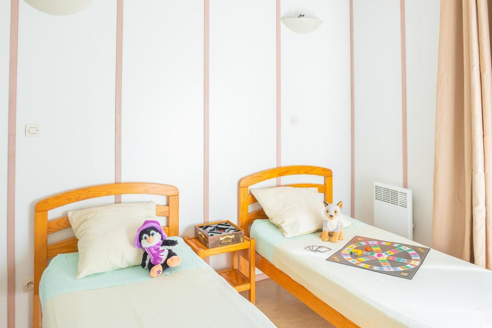 Une chambre avec deux lits simples, chacun doté d’une tête de lit en bois, d’une petite table de chevet et d’un jouet en peluche.