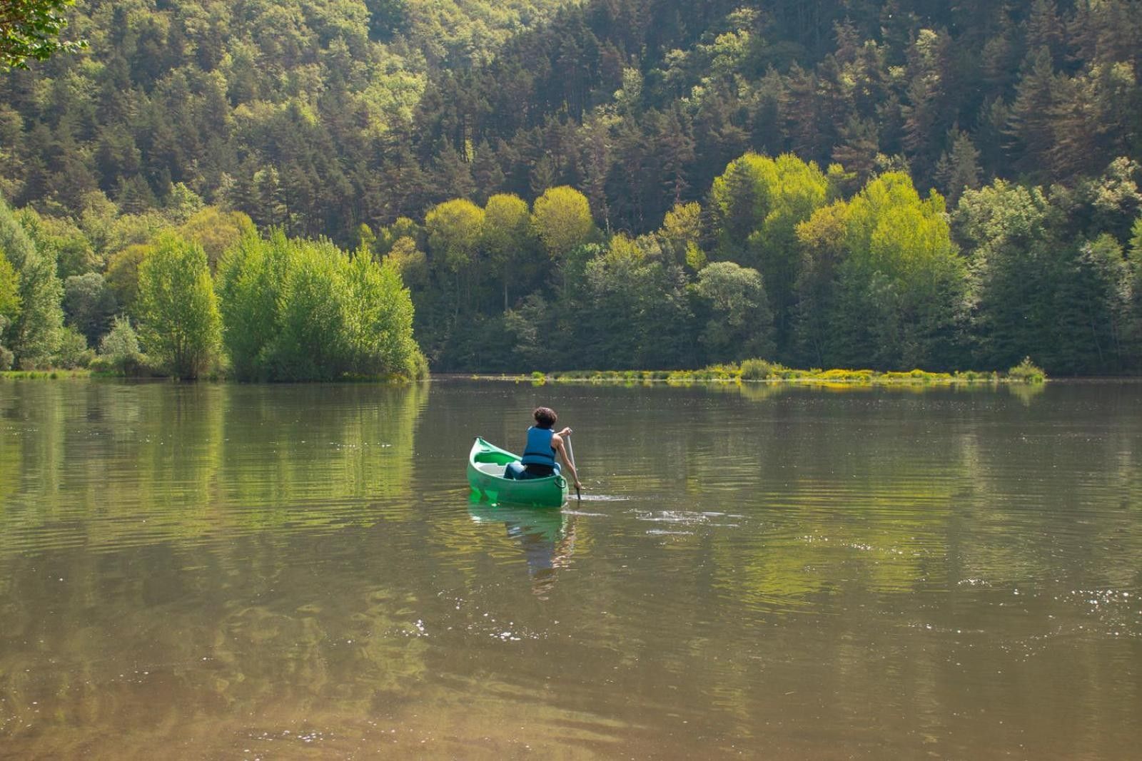 Eine Person in einem grünen Kajak auf einem ruhigen See, umgeben von dichtem Wald.