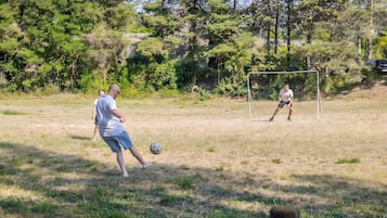 Een buitenveldvoetbalwedstrijd in een grasveld met bomen op de achtergrond.