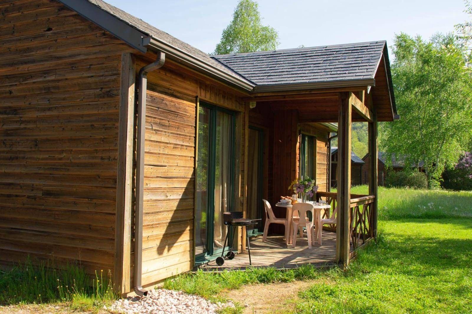 A wooden cabin with a porch, a table, and chairs.