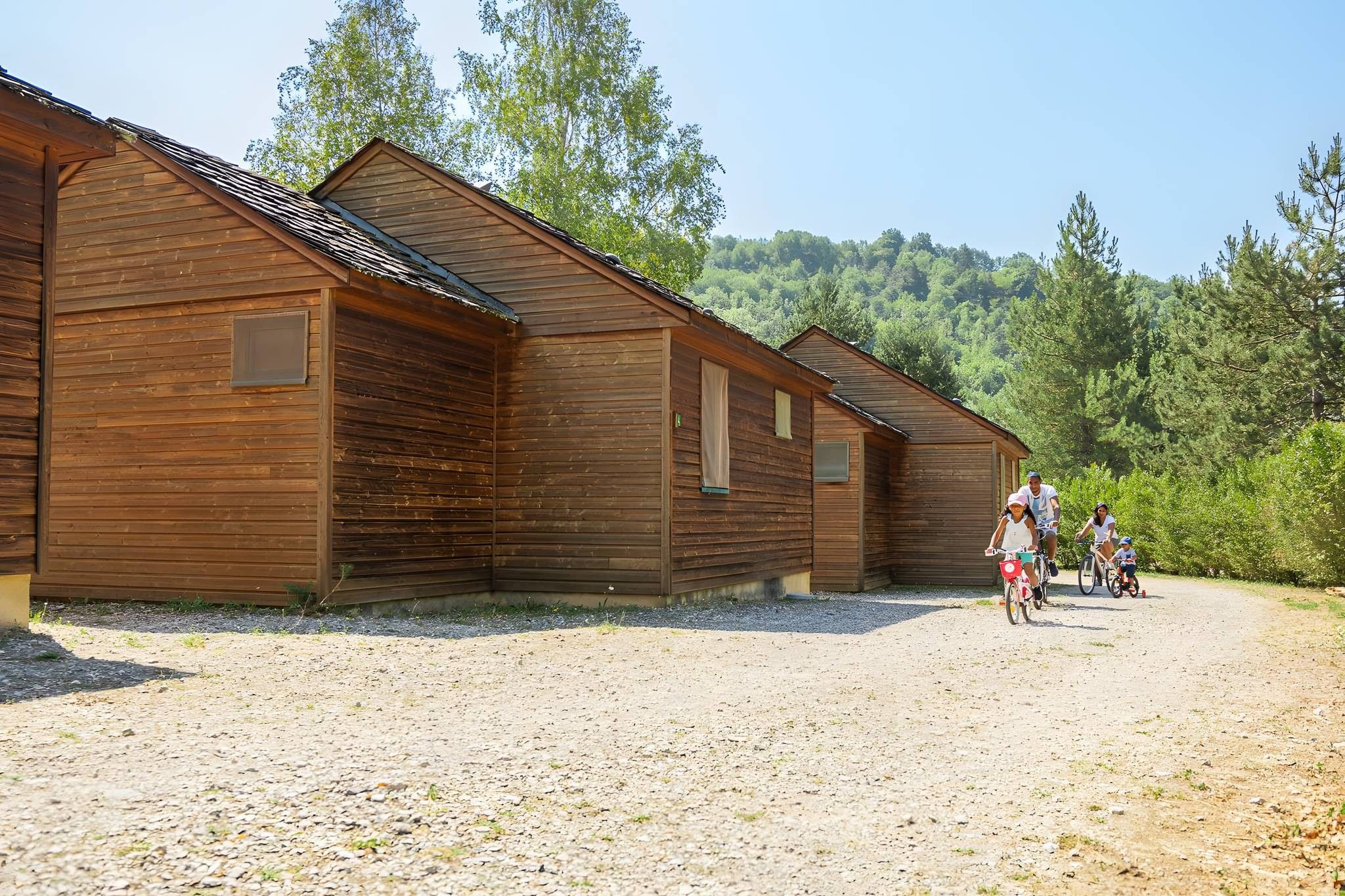 Un bâtiment en bois, avec une allée de gravier et une colline boisée en arrière-plan.