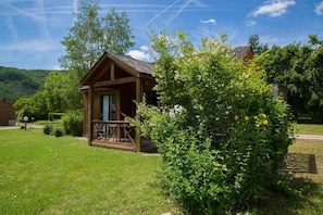 A wooden cabin with a porch, surrounded by lush greenery and a clear sky.