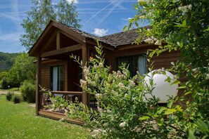 Une cabane en bois dotée d’un porche, entourée de verdure et sous un ciel dégagé.