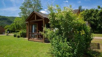 Une cabane en bois dotée d’un porche, entourée d’une végétation luxuriante et sous un ciel dégagé.