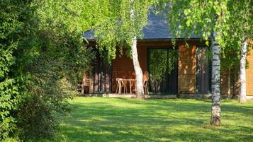 A wooden cabin with a covered patio area, surrounded by lush greenery.