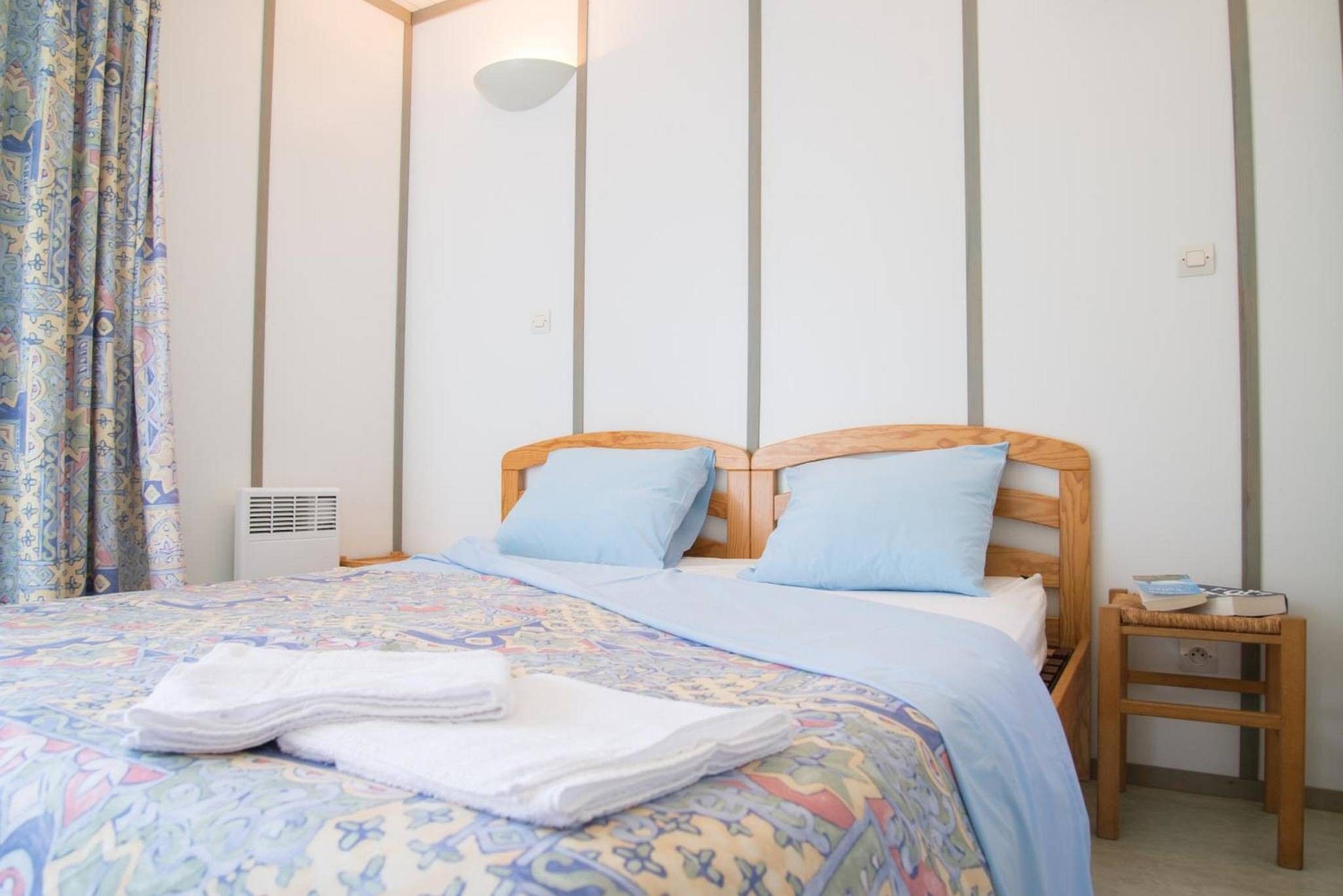 Een net opgemaakt bed met een beddekleed met patroon, twee kussens en een opgevouwen handdoek.