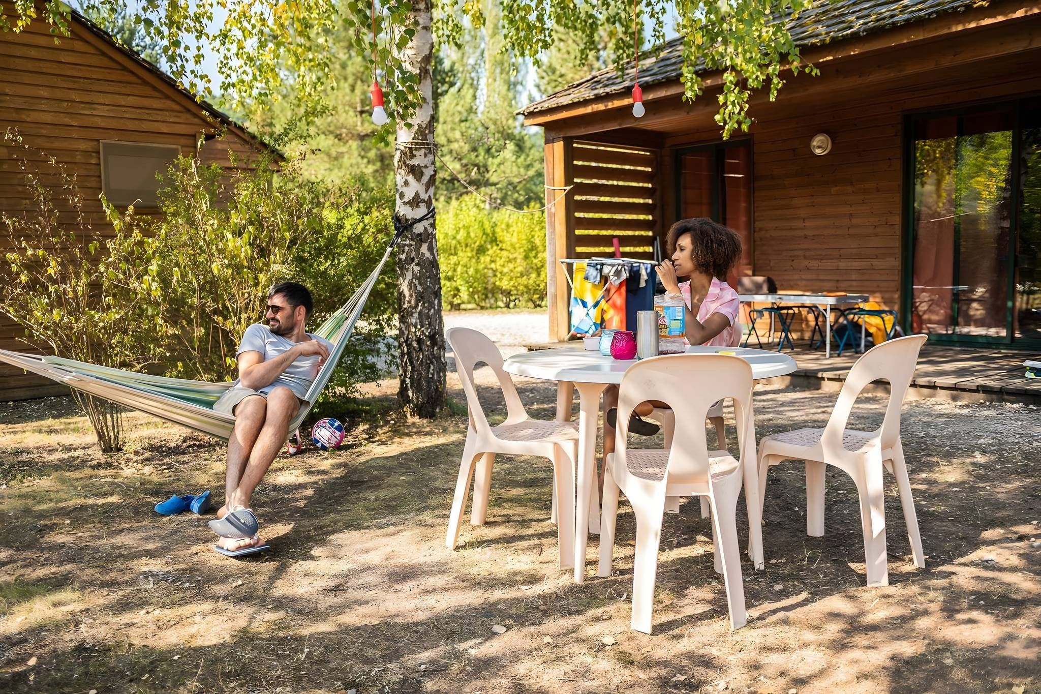 Una cabaña de madera con una hamaca, una mesa al aire libre, sillas y una pelota de voleibol.