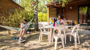 Una cabaña de madera con una hamaca, una mesa al aire libre, sillas y una pelota de voleibol.