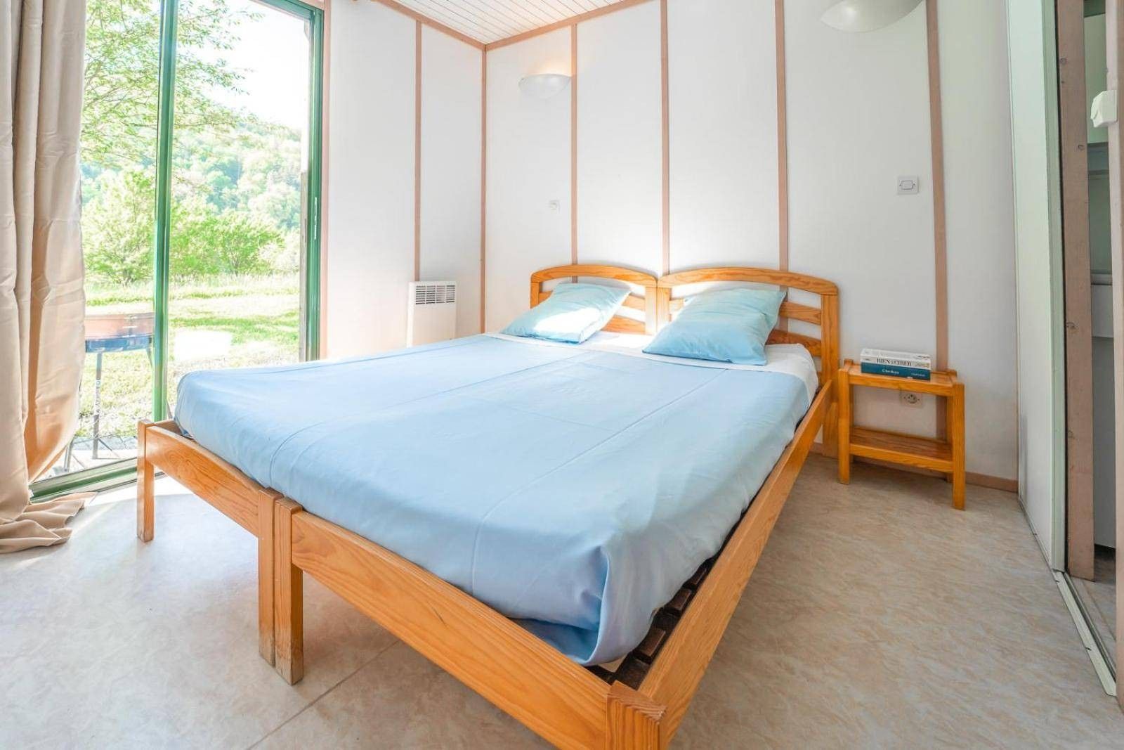 Une chambre à coucher avec un lit en bois, une table de chevet et une fenêtre avec des rideaux.