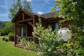Une cabane en bois dotée d’un porche, entourée de verdure et sous un ciel dégagé.