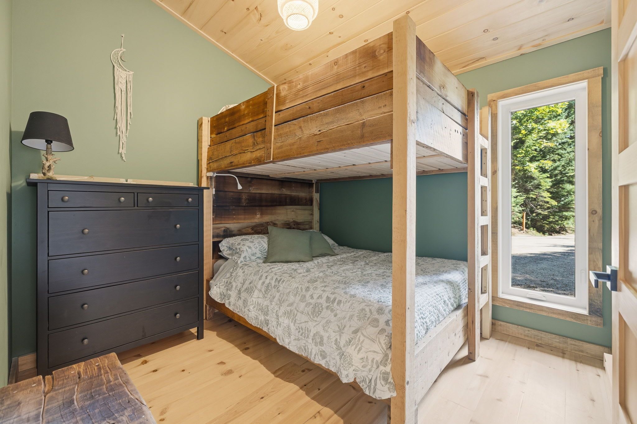 Ein Zimmer mit Etagenbett, Kommode und Fenster mit Blick auf Grünflächen.