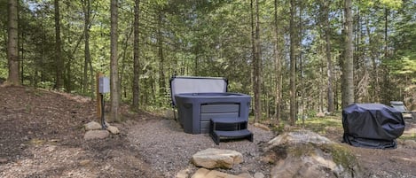 A campsite with a portable heater, a grill, and a picnic table surrounded by trees.