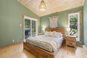 Een slaapkamer met een houten bed, een macramé wanddecoratie en uitzicht op het landschap door een raam.