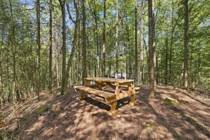 A wooden picnic table in a forest with tall trees. - Spa & Nature Escape | L'Ame des Bois (Grenville-sur-la-Rouge)