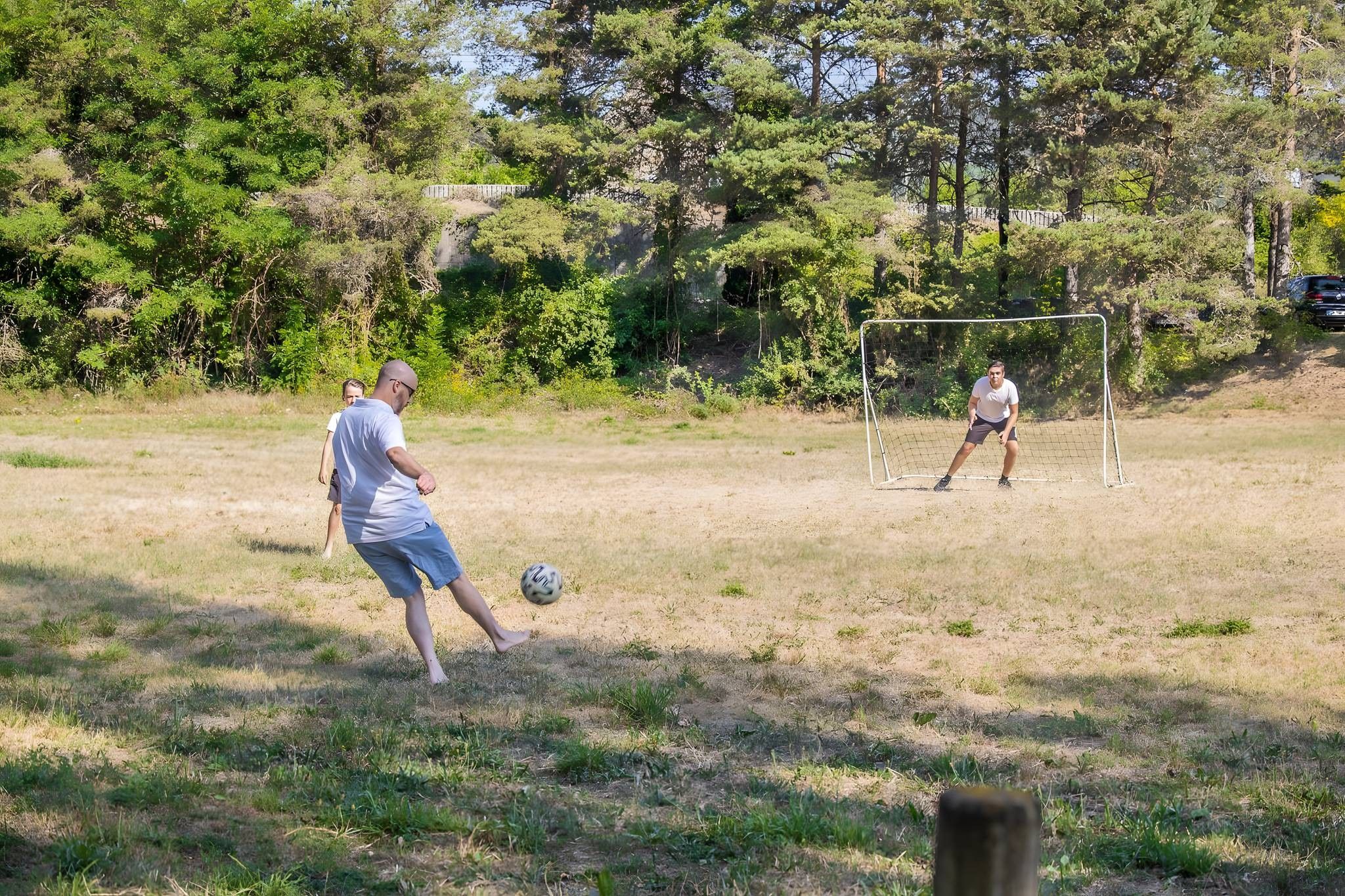 Een buitenveldvoetbalwedstrijd in een grasveld met bomen op de achtergrond.