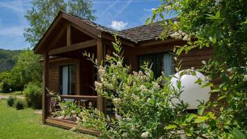 Une cabane en bois dotée d’un porche, entourée de verdure et sous un ciel dégagé.