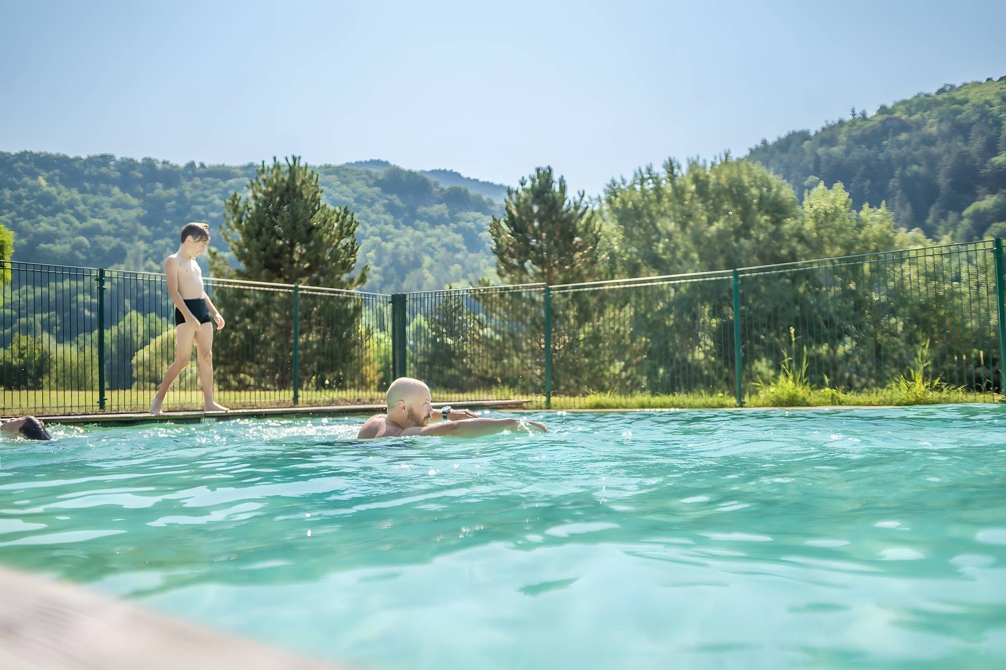 Une piscine à l’eau claire, entourée d’une clôture et d’arbres.