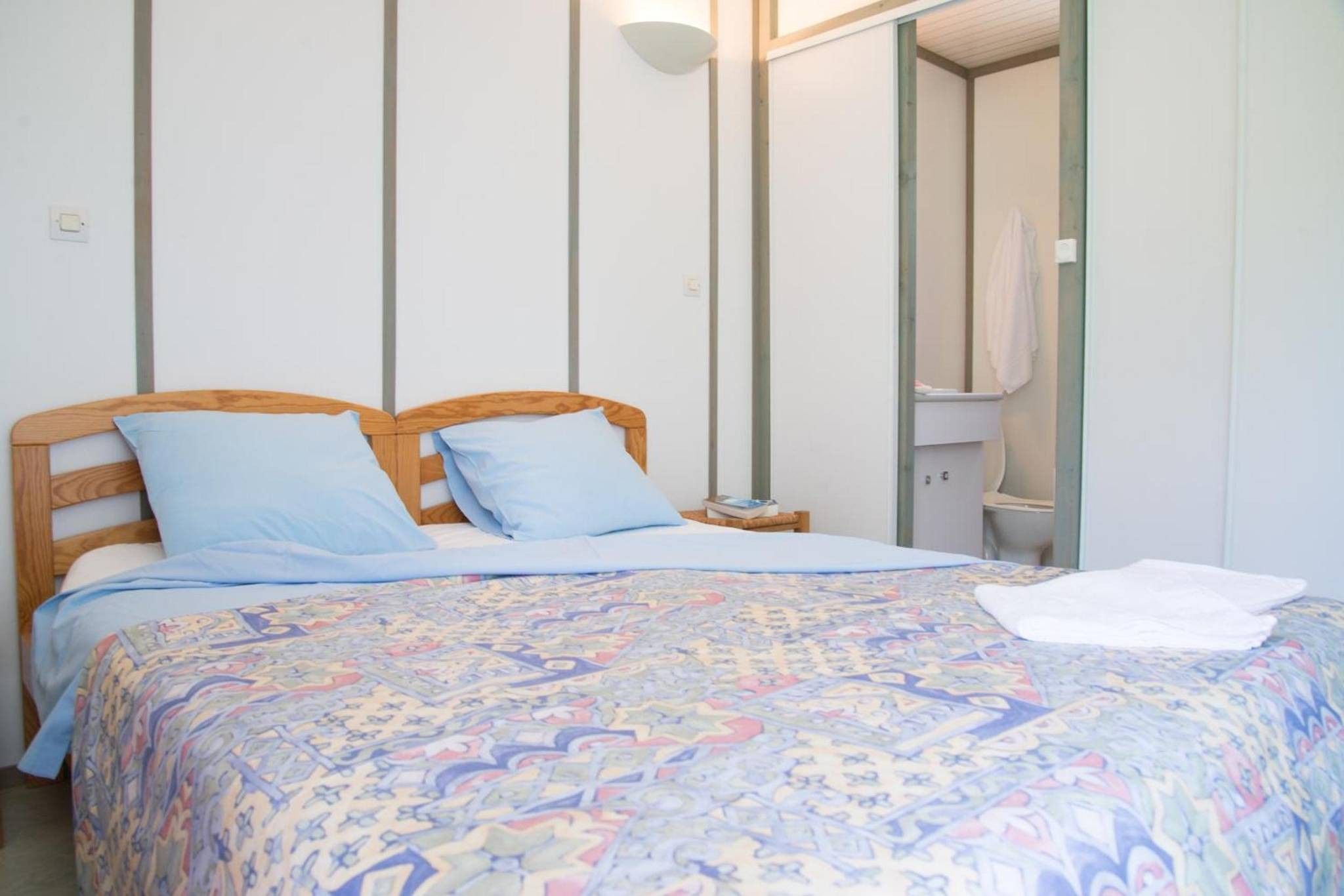Ein Bett mit einem gemusterten Überwurf, einem Holz-Kopfteil und zwei Kissen.