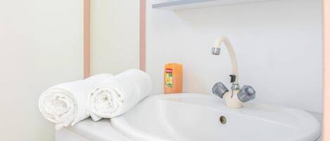 A bathroom sink with two rolled towels and a bottle of soap.