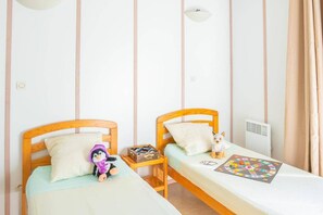 Un dormitorio con dos camas individuales, una mesita con un juego de mesa y un peluche sobre una cama.