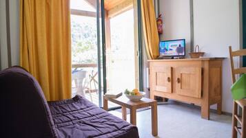 Een kamer met een bank, een houten kast, een televisie en een raam met gordijnen.