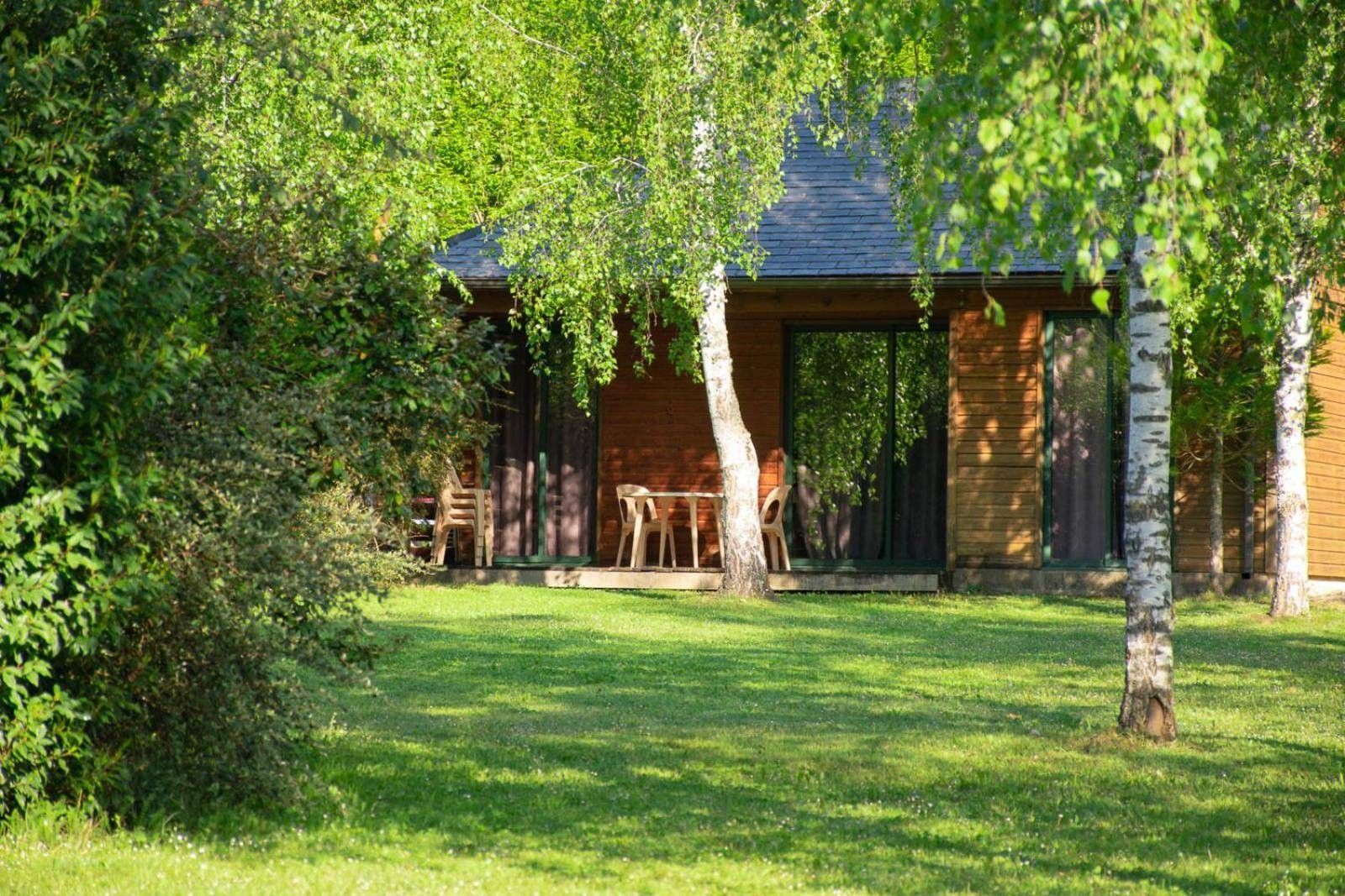 En træhytte med en overdækket terrasse, omgivet af frodig vegetation.