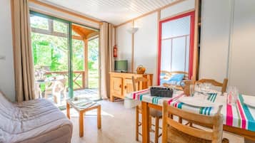 A room with a bed, a dining table set for two, a television, and a view of greenery outside.