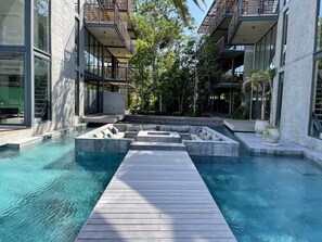 A modern pool area with a wooden deck, surrounded by buildings with large windows and balconies. - Xalet 307a Tulum Cenote y Beach Club Privileges (Tulum)