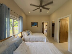 A bedroom with two beds, a ceiling fan, and a window with curtains. - Three Harbour Villa in Samaan Grove (Canaan, Tobago)