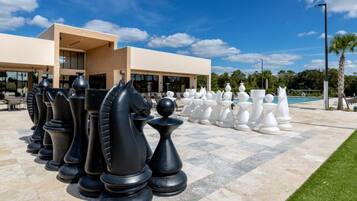 A chessboard with large chess pieces set up outdoors, a building in the background, and a clear sky.