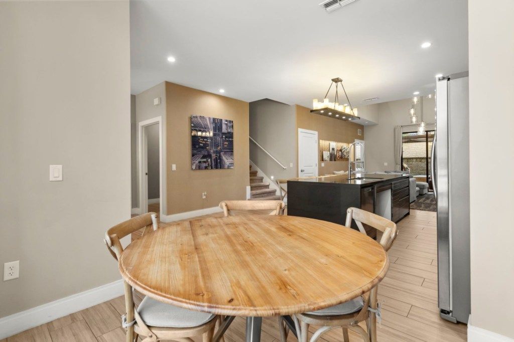 Une cuisine moderne dotée d’un îlot central, un coin repas avec une table et des chaises en bois rond, et un escalier menant à un niveau supérieur.