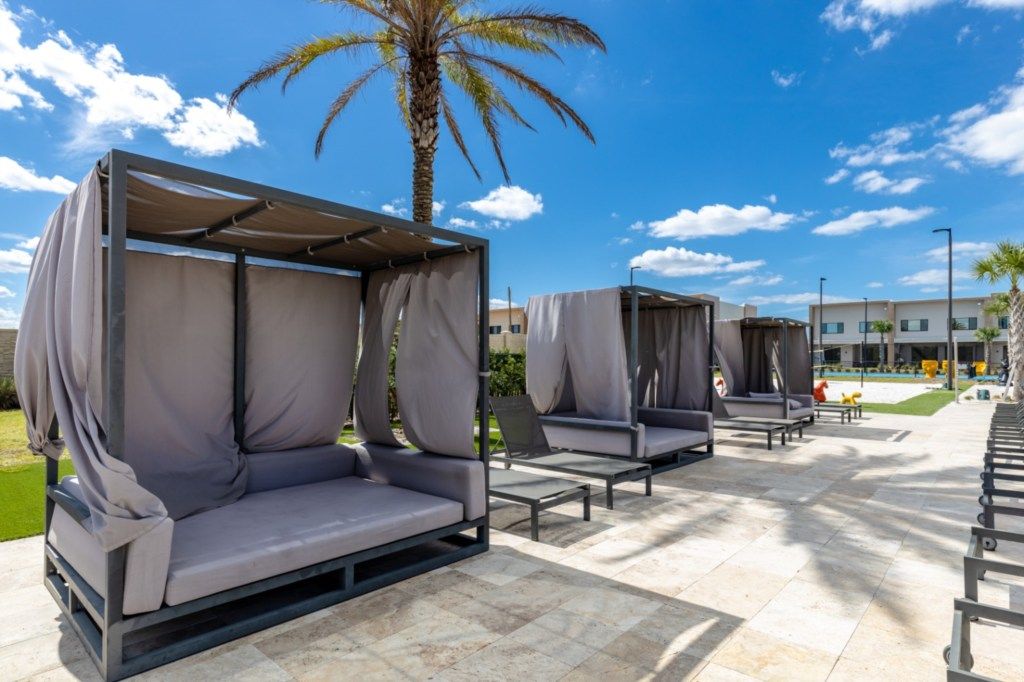 Zonas de estar al aire libre con sillones cubiertos, una palmera y un edificio al fondo.