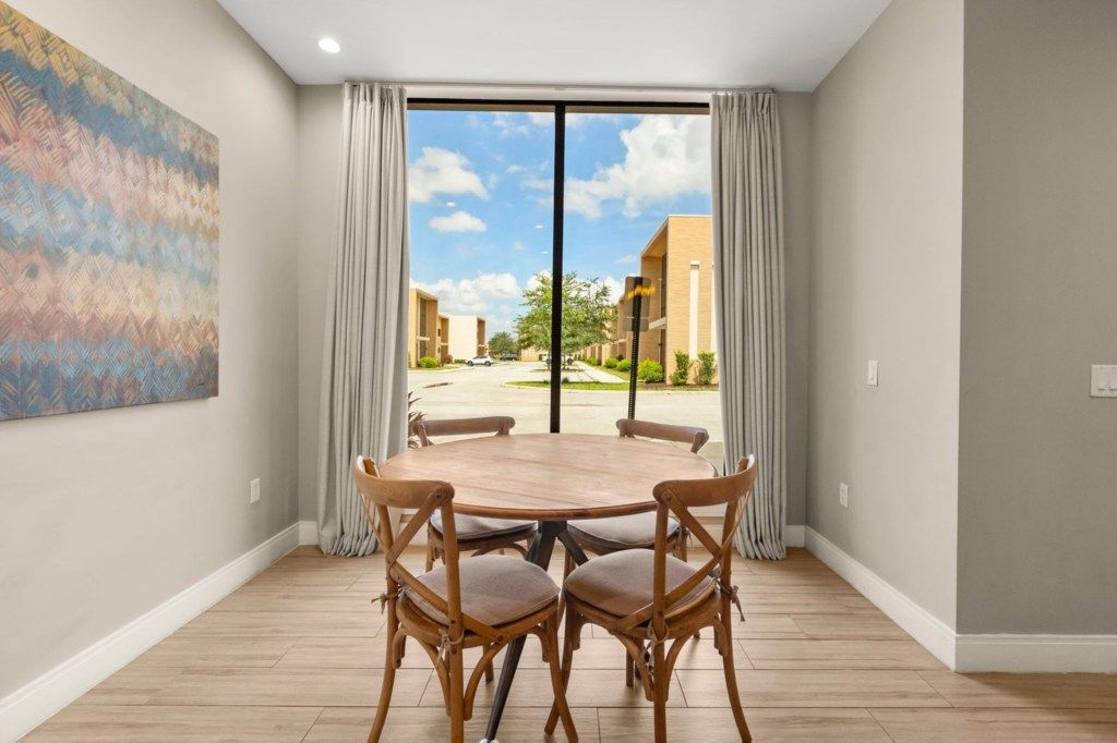 Una habitación con una mesa de comedor y sillas, un ventanal con cortinas y un cuadro en la pared.