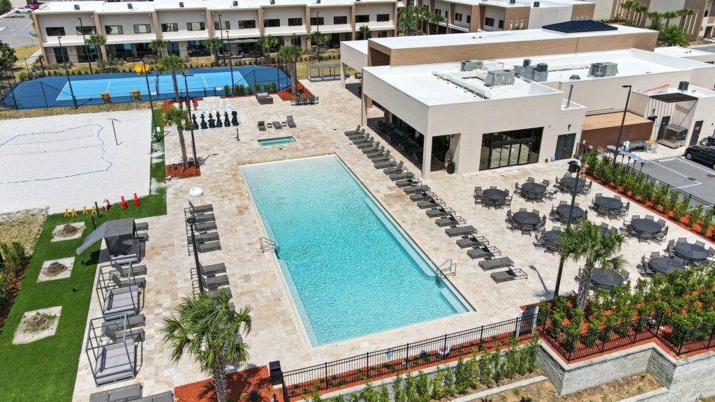 Una piscina con sillones de descanso y una cancha de tenis.