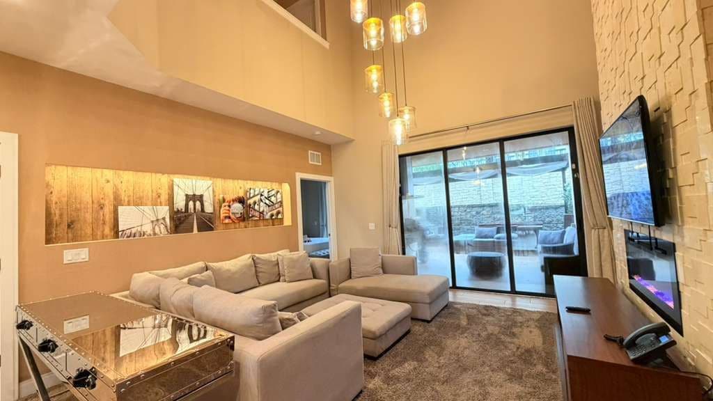 A modern living room with a sectional sofa, a flat-screen TV, and a large window offering a view of the outdoors.
