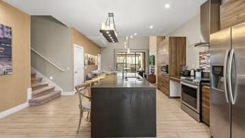 A modern kitchen with a central island, stainless steel appliances, and a staircase leading to another level.