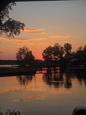Ein Sonnenuntergang über ruhigem Gewässer mit Bäumen und einem Steg.